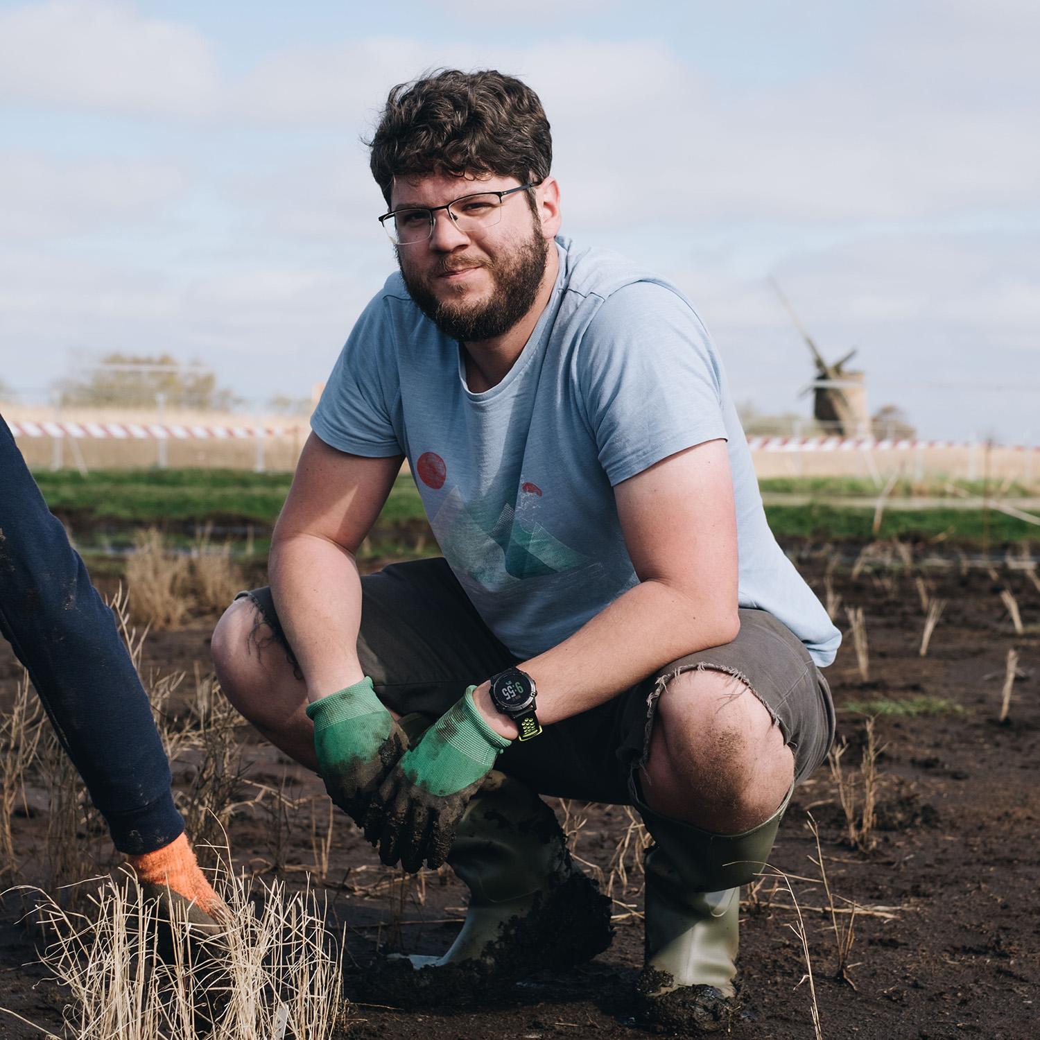 A volunteer crouching down as he plants small reed plants at Horsey