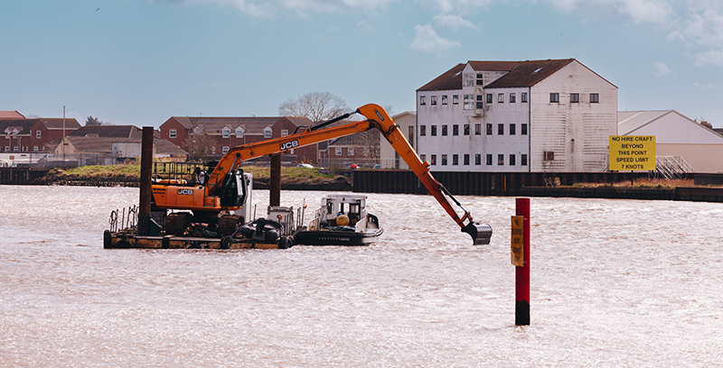 A dredging rig busy at work in an open body of water near great yarmouth, with buildings visible in the background