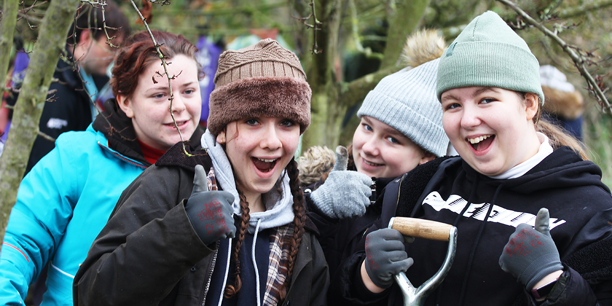 Young people doing conservation work outdoors during the first Generation Green project giving the thumbs up